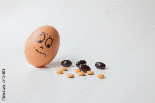 Close up of egg with doubtfully and 
disapproving face watching at a group of tablets with different color, shape e dimension. White uniform paper background. Idea of addiction to drugs. photo