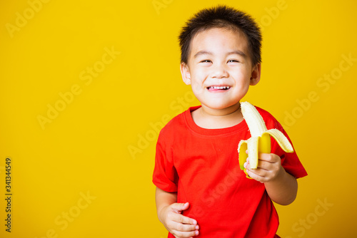 kid cute little boy attractive smile wearing red t-shirt playing holds peeled banana for eating