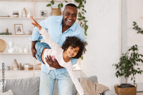 Family playtime. Happy African American grandfather playing silly game with his granddaughter at home, blank space