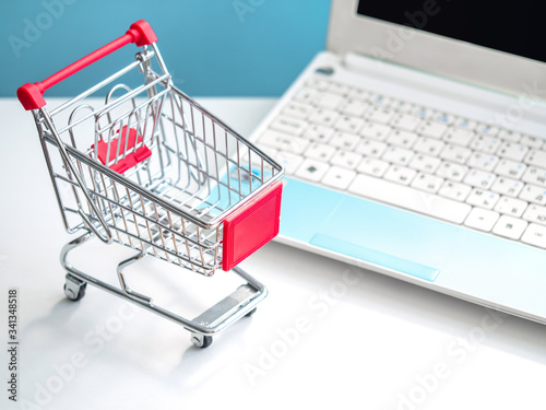 Shopping cart and portable computer. Safe and online shopping on coronavirus quarantine concept. Blue and white background, top view.