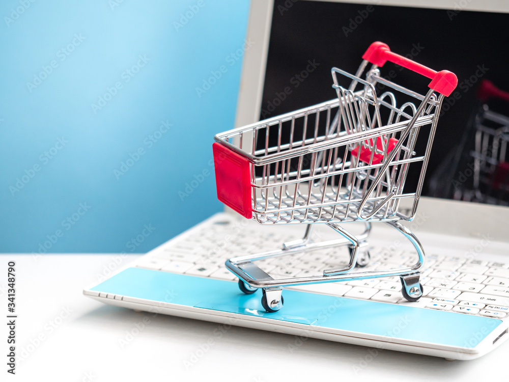 Shopping cart and portable computer. Safe and online shopping on coronavirus quarantine concept. Blue and white background, copy space.