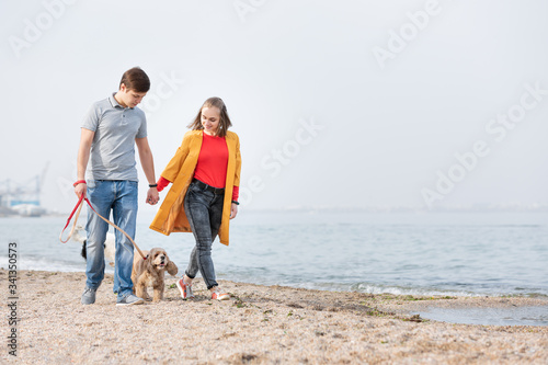 Young couple walking with a dog on a sea coast. Dog walking outdoors.