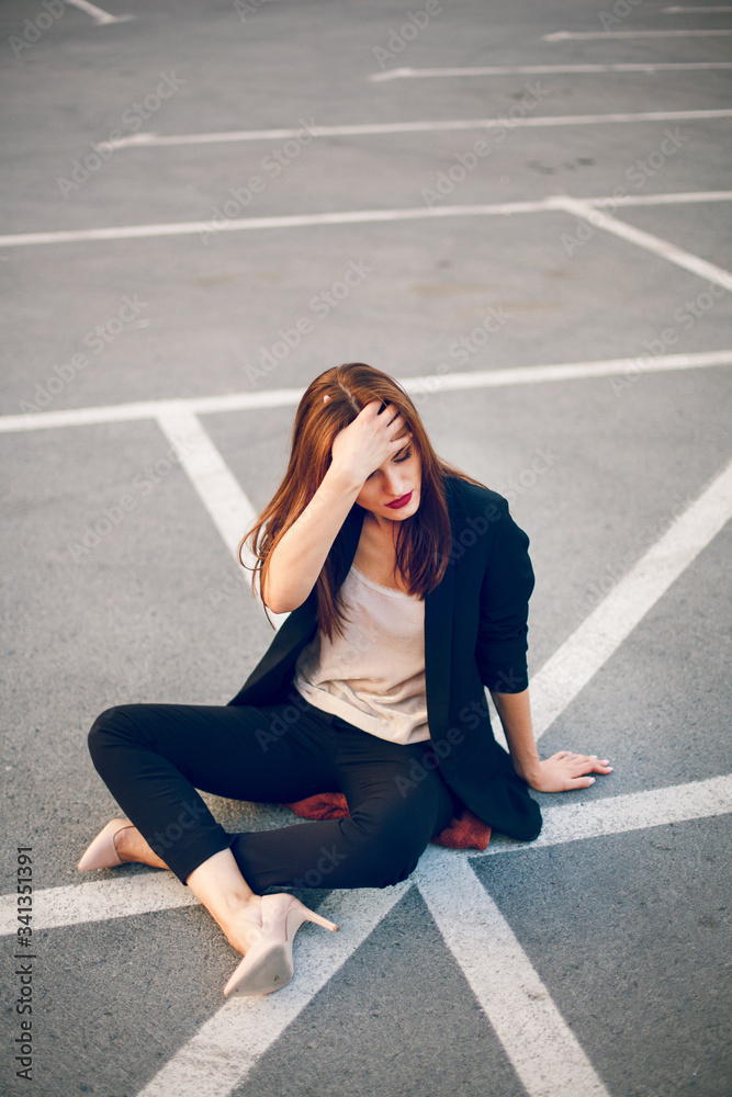 Red-haired model in a suit sits in a parking lot in summer Red-haired model in a suit sits in a parking lot in summer