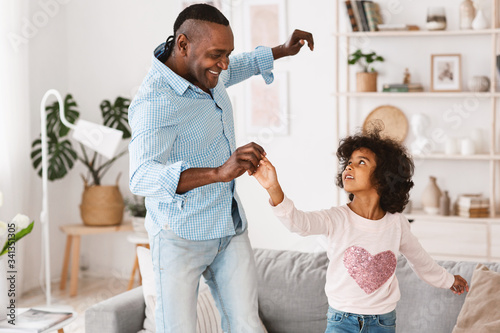 Stay home, have fun. African American granddad dancing with little granddaughter in light room
