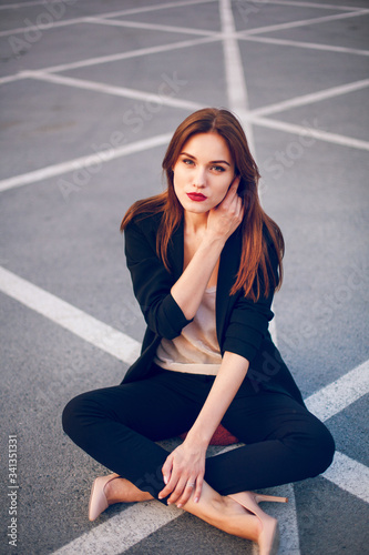 Red-haired model in a suit sits in a parking lot in summer