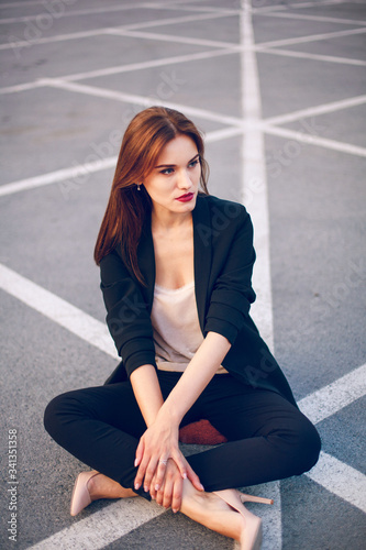 Red-haired model in a suit sits in a parking lot in summer