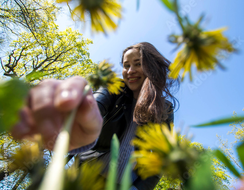 Girl picking dandelion flower in field of grass, low angle of flower stem being picked by beautiful young energetic girl, spring/summer colors, flower field, fun in the park and nature, POV ground