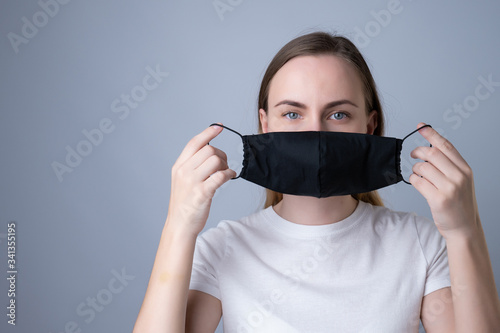 Woman puts a black medical mask on her face on a gray background