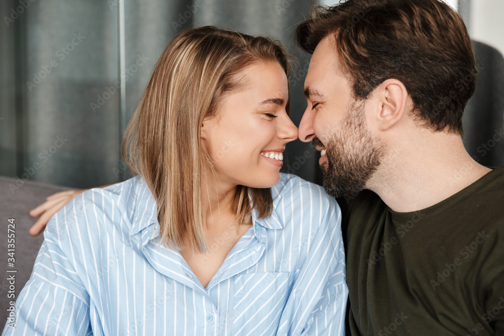 Photo of cheerful couple laughing and hugging while sitting on sofa Photo of cheerful couple laughing and hugging while sitting on sofa
