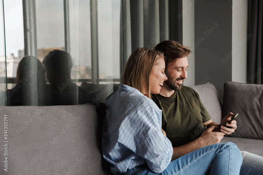 Photo of cheerful beautiful couple laughing and using mobile phone