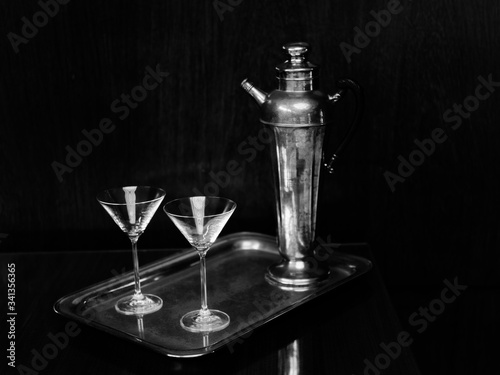 Black and white image of cocktail glasses and antique silver decanter claret jug on a silver plate. photo