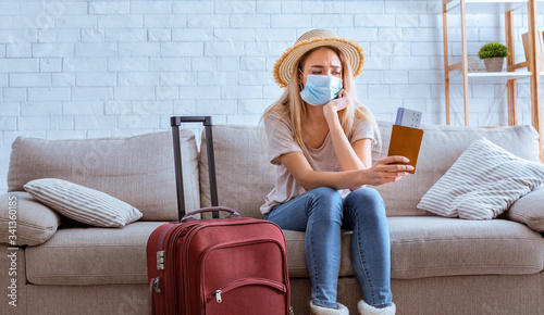 Sad girl in mask with tickets and suitcase photo