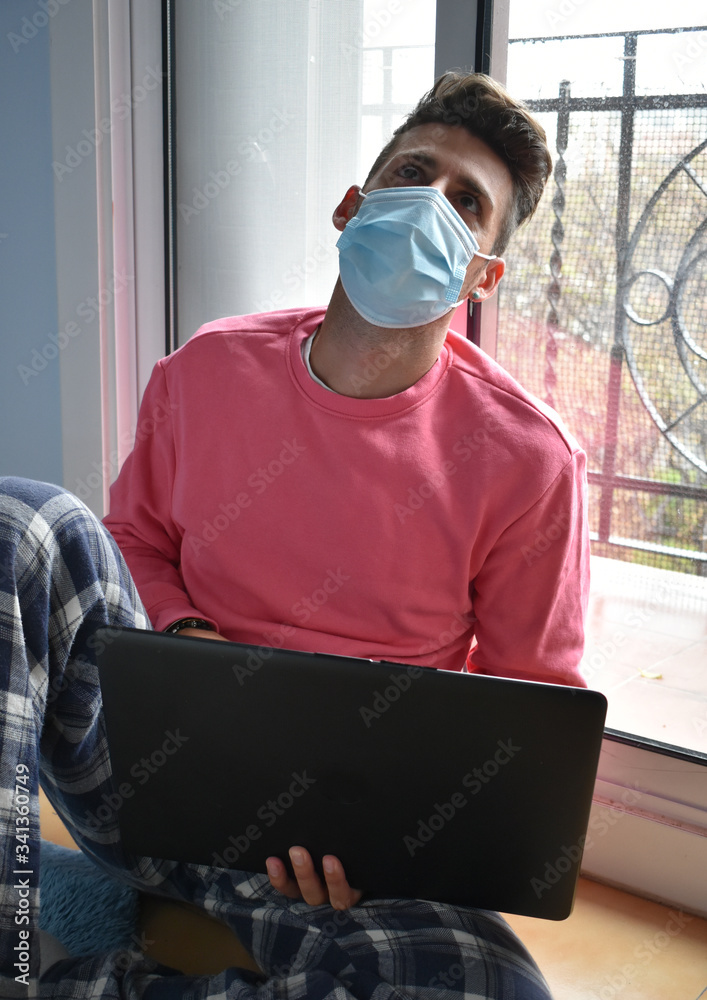 Young man in quarantine working from home with the laptop wearing a surgical mask to protect himself from the coronavirus Young man in quarantine working from home with the laptop wearing a surgical mask to protect himself from the coronavirus