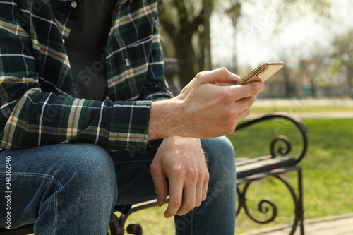Man uses smartphone sitting on bench in park
