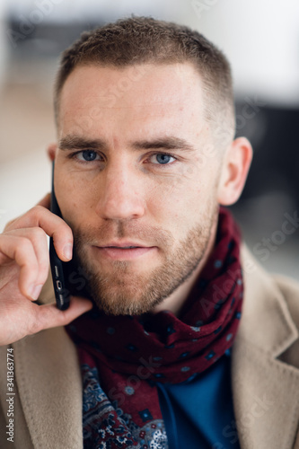 Young serious man wearing scarf and coat talking on mobile phone close-up.