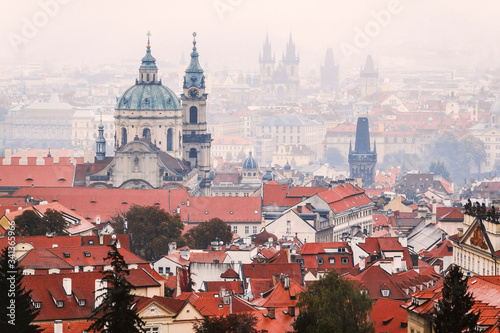 Scenic view of Prague tiled roofs during cloudy and foggy weather. Postcard concept. St. Nicholas church seen from Petrin hill viewpoint. Beautiful panoramic picture of the city. Czech Republic.