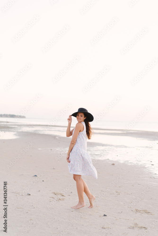 Girl in a hat walks on the beach