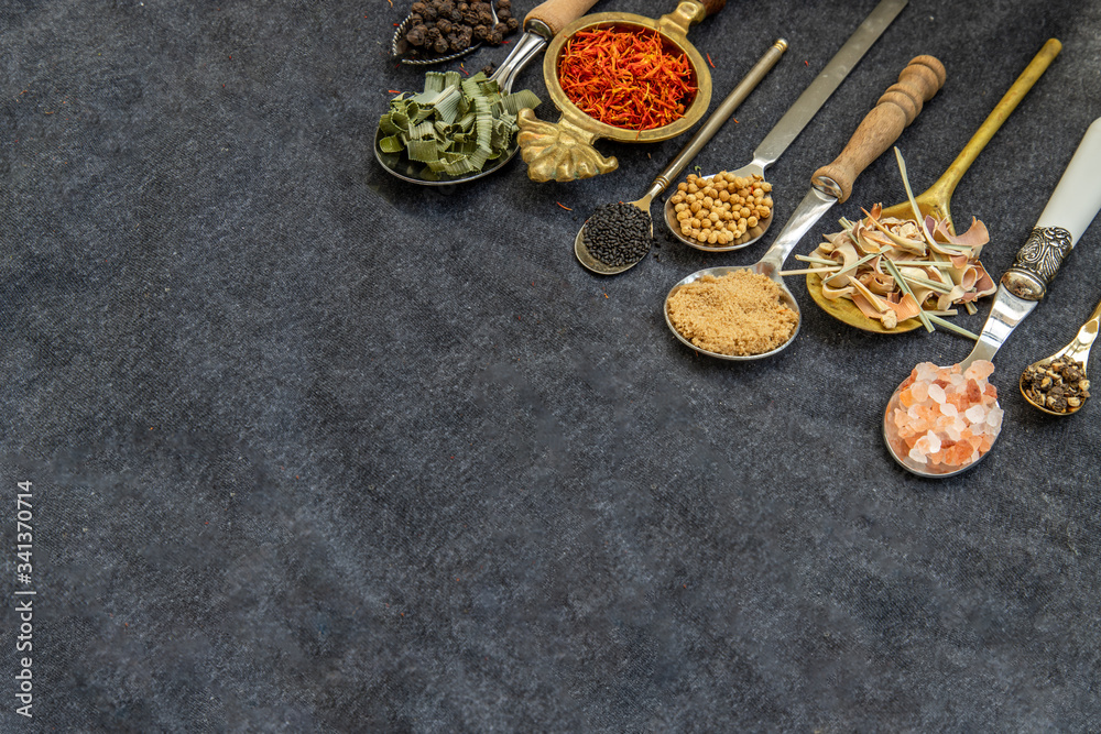 Various teas and dried herbs assortment on spoons in rustic style on balck background.