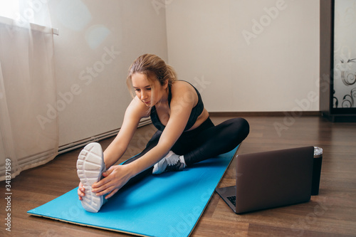 Young woman exercising at home in a living room. Video lesson. Young woman repeating exercises while watching online workout session. Beautiful young woman doing fitness exercise at home