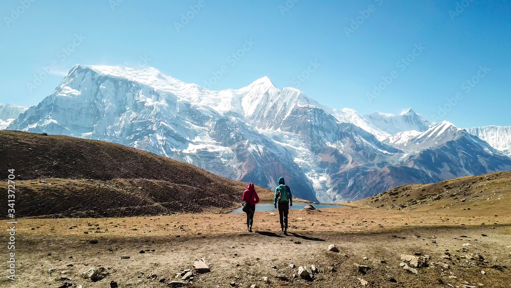 A couple walking towards the Ice lake, along Annapurna Circuit Trek, Himalayas, Nepal. Snow caped Annapurna chain in the back. Clear weather, dry grass, snowy peaks. High altitude trekking. Freedom A couple walking towards the Ice lake, along Annapurna Circuit Trek, Himalayas, Nepal. Snow caped Annapurna chain in the back. Clear weather, dry grass, snowy peaks. High altitude trekking. Freedom