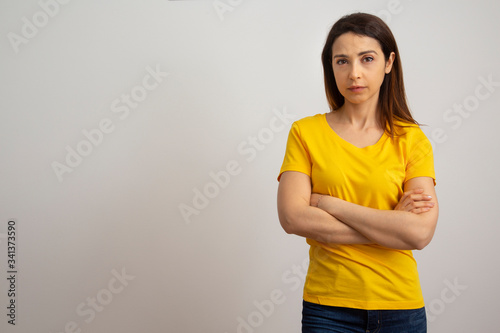 Donna mora con una maglietta Gialla e Jeans a braccia conserte su sfondo bianco