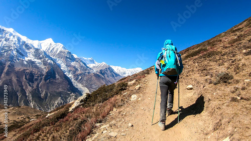 A man trekking on the Annapurna Circuit Trek, Himalayas, Nepal. Panoramic view on snow caped Annapurna chain. Lots of dried grass. High altitude, massive mountains. Freedom and adventure