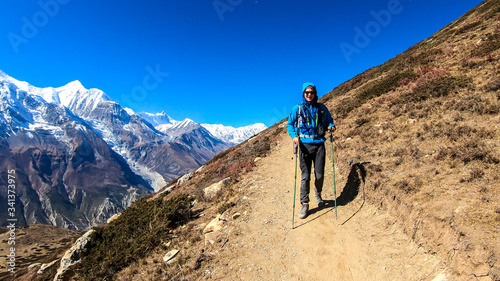 A man trekking on the Annapurna Circuit Trek  Himalayas  Nepal. Panoramic view on snow caped Annapurna chain. Lots of dried grass. High altitude  massive mountains. Freedom and adventure