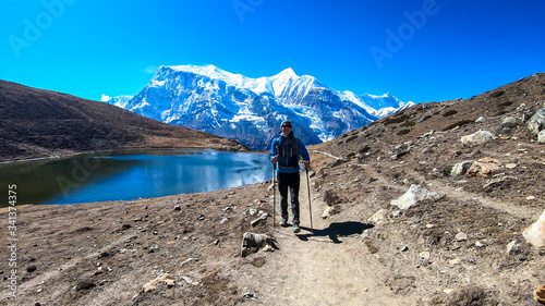 A man trekking along the Ice Lake  Annapurna Circuit Trek detour  Himalayas  Nepal  surrounded by high  snow caped mountains. Annapurna Chain in the back. High altitude lake. Harsh landscape.