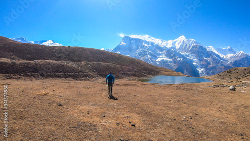 A man trekking towards Ice Lake, Annapurna Circuit Trek in Himalayas, Nepal, surrounded by high, snow caped Annapurna Chain in the back. High altitude lake. Harsh landscape. He is enjoying the view