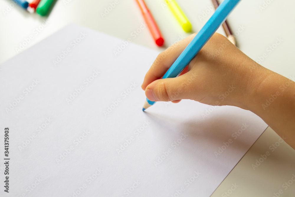 Close up of child's hands drawing at blank white paper with a blue pencil Close up of child's hands drawing at blank white paper with a blue pencil
