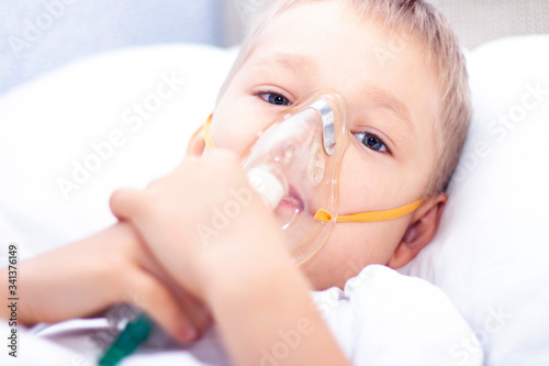 boy with an inhaler mask - respiratory problems in asthma. a boy with an inhaler mask lies in bed and breathes adrenaline. healthcare concept and sick child, coronavirus, bronchitis, pneumonia