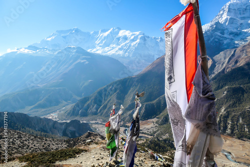 A row of waving flags with mantra "Om mani padme hum" on them. Wind blows them over Himalayan peaks. Very weary flags. In the back here is snow caped Annapurna Chain. Meditation and retreat