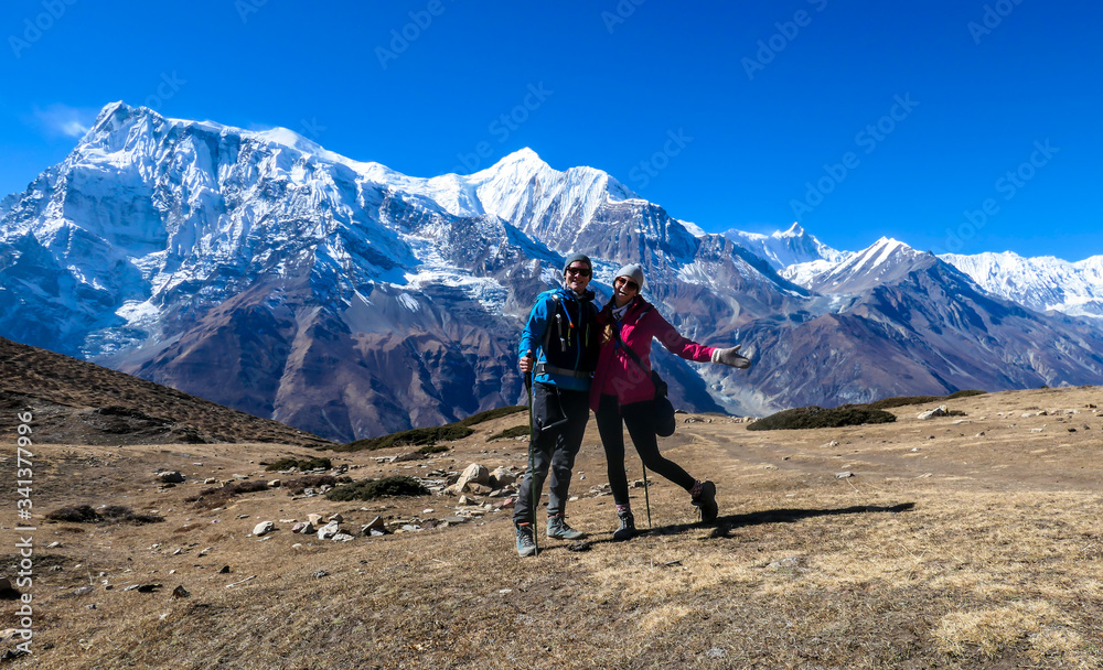 A couple hugging along the Annapurna Circuit Trek, Himalayas, Nepal. Panoramic view on snow caped Annapurna chain. Lots of dried grass. High altitude, massive mountains. Love and cheerful moments