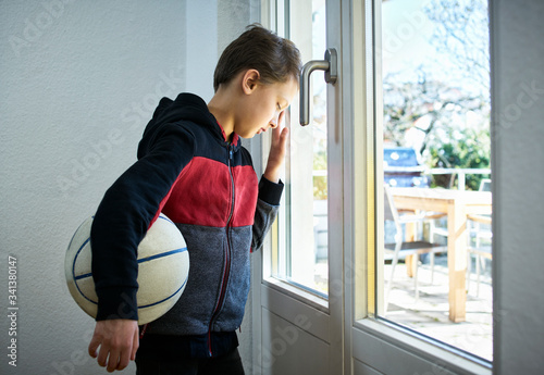 Sad boy with basketball leaning against the window photo