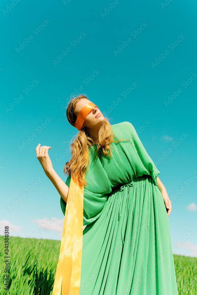 Blindfolded young woman wearing a green dress standing in a field Blindfolded young woman wearing a green dress standing in a field