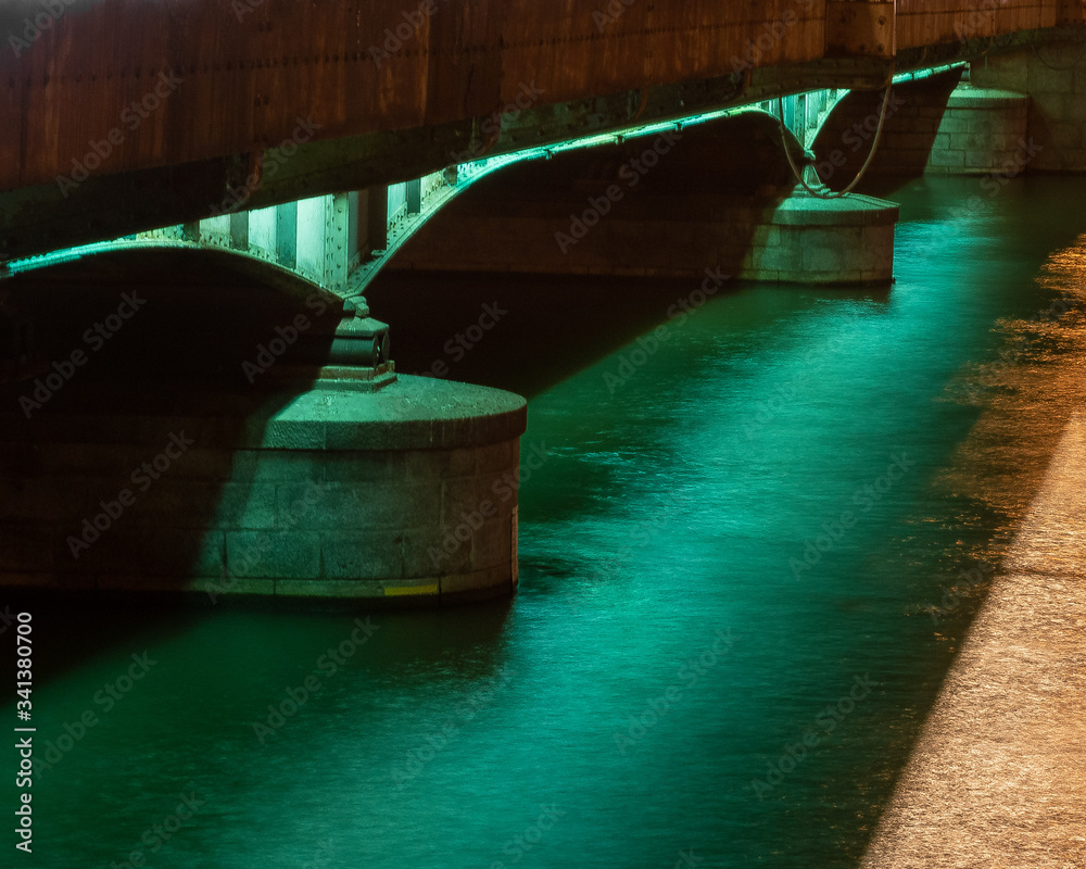 Bridge illuminated with a green light underneath.  Still water with green tint. Wroclaw, Poland.