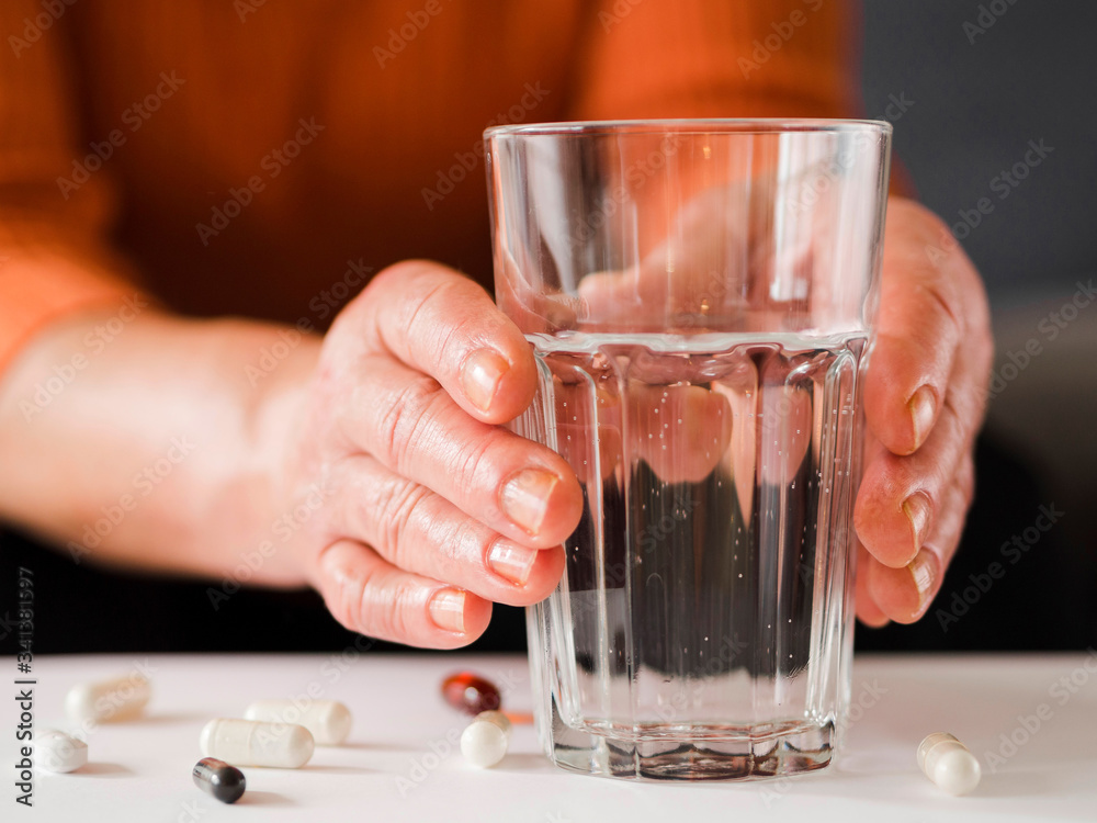 Close-up patient holding glass and capsules on table Close-up patient holding glass and capsules on table