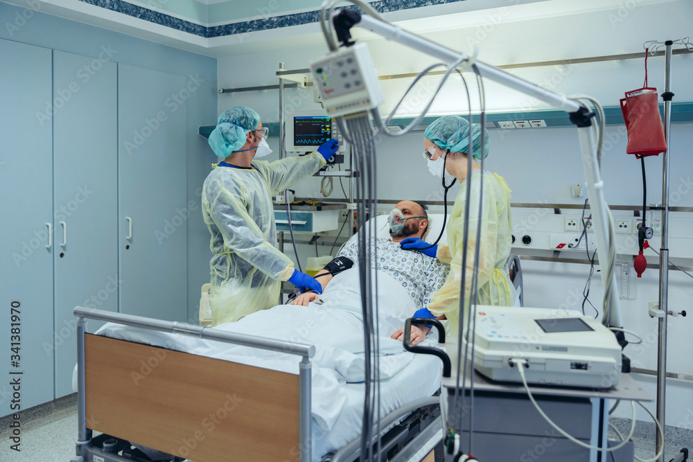 Doctors caring for patient in emergency care unit of a hospital looking at screen Doctors caring for patient in emergency care unit of a hospital looking at screen