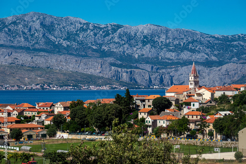 Red roofs of village Postira on island Brac in Croatia with green playground in front and mountain Mosor in background