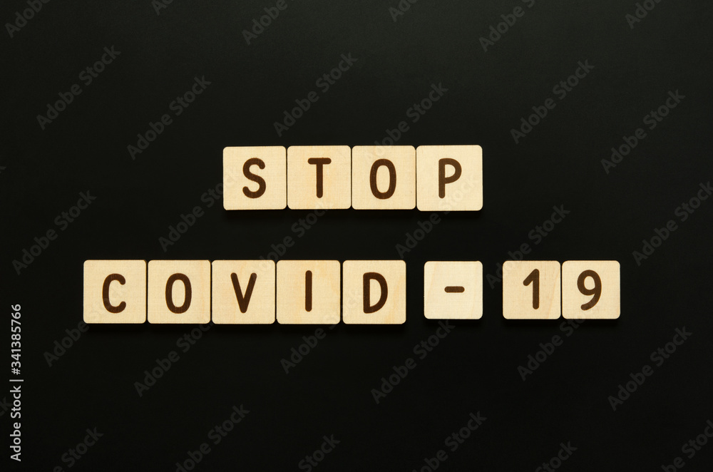 Stop COVID-19 - word from wooden blocks with letters. Top view on black background. - Image Stop COVID-19 - word from wooden blocks with letters. Top view on black background. - Image