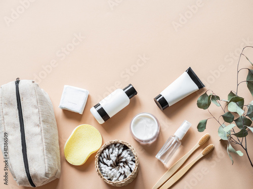 Travel cosmetic bag with the necessary means to care for women's skin. Cosmetics, dry shampoo, cotton buds, toothbrushes next a cosmetic bag on a beige background. top view