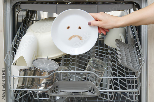 Poorly washed dishes in the dishwasher. Integrated Dishwasher with white plates front vew and sad emotion on plate. broken dishwasher machine concept photo