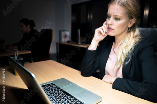 An caucasian office worker is working overtime at the office, She is stressed and tired.