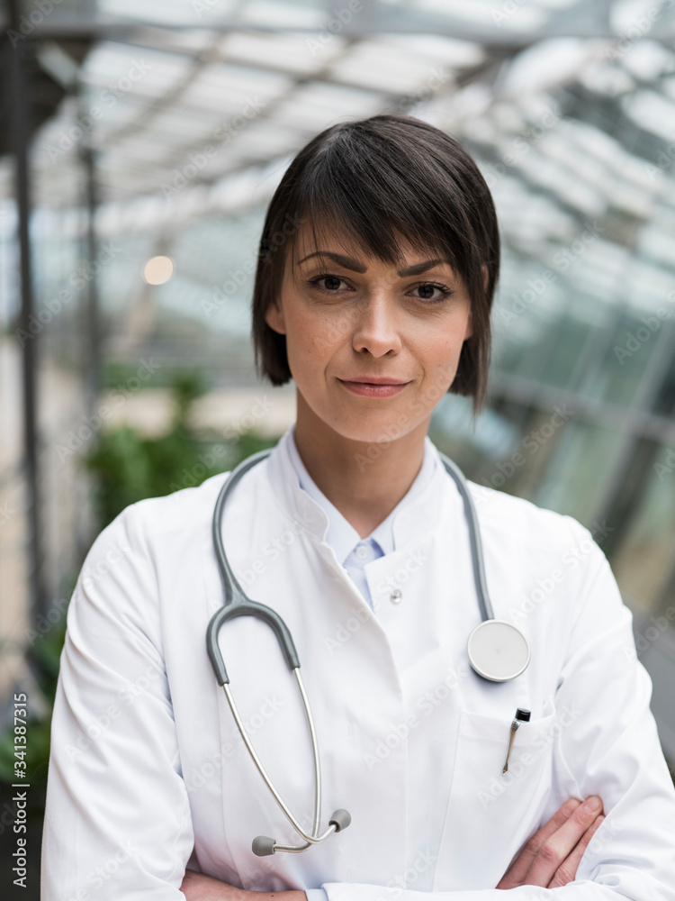 Portrait of femeale doctor with stethoscope, standing in atrium, with arms crossed Portrait of femeale doctor with stethoscope, standing in atrium, with arms crossed