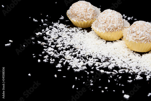 White coconut balls, raw and healthy sugar free rafaello candies on black glass background. Covering balls in coconut shred. Vegan, vegetarian sweets photo