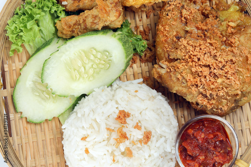 Ayam penyet a East Javanese cuisine smashed fried chicken dish with floss sambal slices of cucumbers fried tofu and tempeh photo