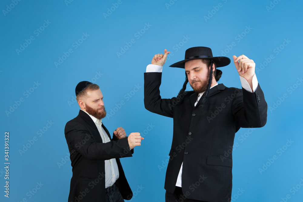 Dancing, having fun. Portrait of a young orthodox jewish men isolated on blue studio background. Purim, business, festival, holiday, celebration Pesach or Passover, judaism, religion concept. Dancing, having fun. Portrait of a young orthodox jewish men isolated on blue studio background. Purim, business, festival, holiday, celebration Pesach or Passover, judaism, religion concept.