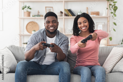 Cheerful black guy and girl playing video games at home