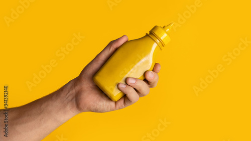 Obraz na plátně Unrecognizable guy holding bottle of mustard on orange background, space for your design