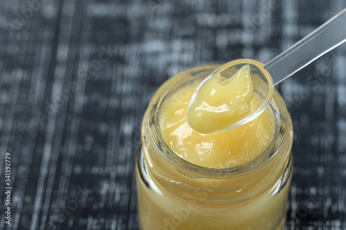 Raw organic royal jelly in a small bottle with litte spoon on small bottle on black background,